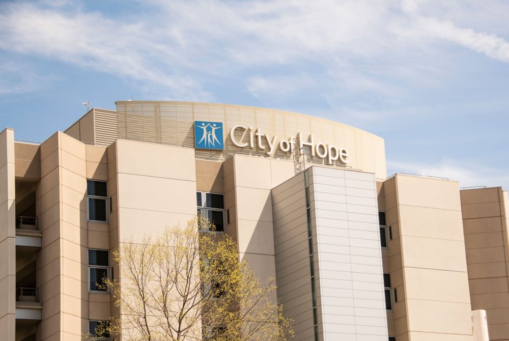 Article Banner - A hospital building with a tan facade and a sign reading "City of Hope" stands against a blue sky with clouds.
