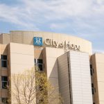 Article Banner - A hospital building with a tan facade and a sign reading "City of Hope" stands against a blue sky with clouds.