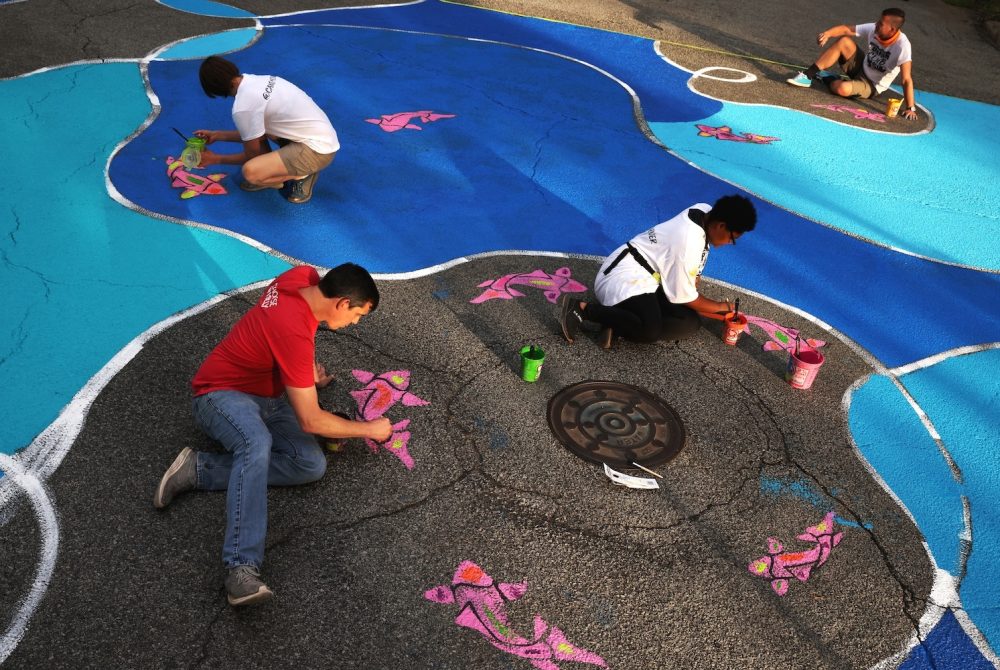 Children making colorful, large-scale art on a city street.