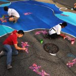 Children making colorful, large-scale art on a city street.