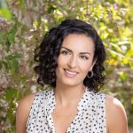 Article Banner - Sabrina Merage Naim stands in front of a plant-filled background wearing a white sleeveless top.