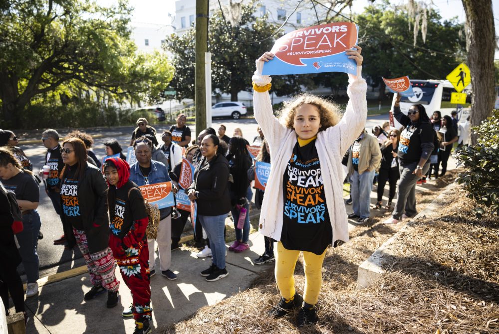 Young woman holding a survivors speak sign at a protest.