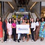 A group of women standing in a conference center or hotel lobby holding a sign.
