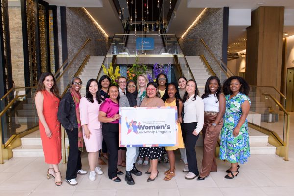 A group of women standing in a conference center or hotel lobby holding a sign.