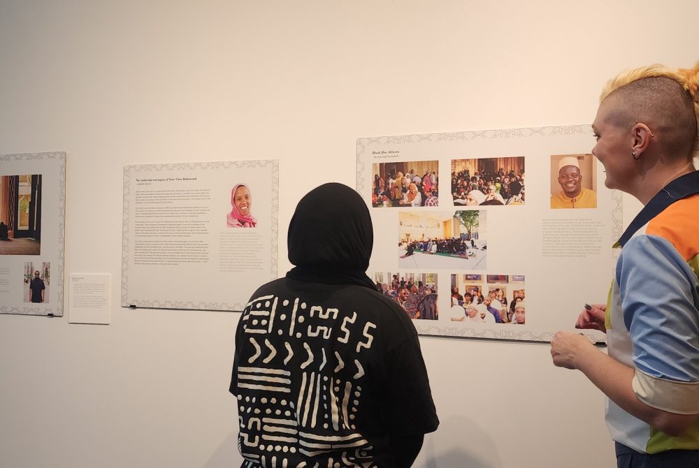 Article Banner - Two people look at photos posted on a white wall with their backs turned to the camera.