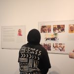Article Banner - Two people look at photos posted on a white wall with their backs turned to the camera.