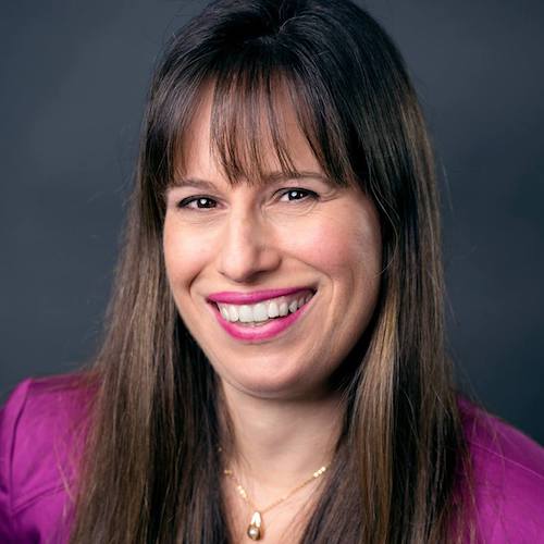 Picture of a smiling woman with long straight brown hair and bangs, wearing a magenta jacket.