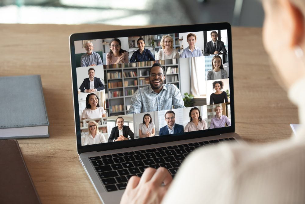 A man looks at a laptop featuring a gallerry-style Zoom screen for a digital meeting.