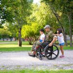Article Banner - A male veteran in a wheelchair out in a park with his two children