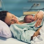 A new mother lies in a hospital bed holding her baby