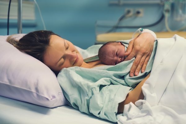 A new mother lies in a hospital bed holding her baby