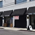 A downtown street with several storefronts, one with a for lease sign.