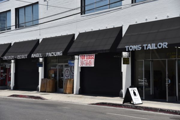 A downtown street with several storefronts, one with a for lease sign.