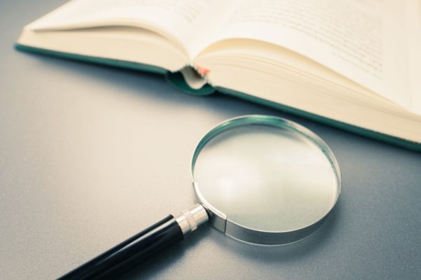 An open book on a table beside a magnifying glass