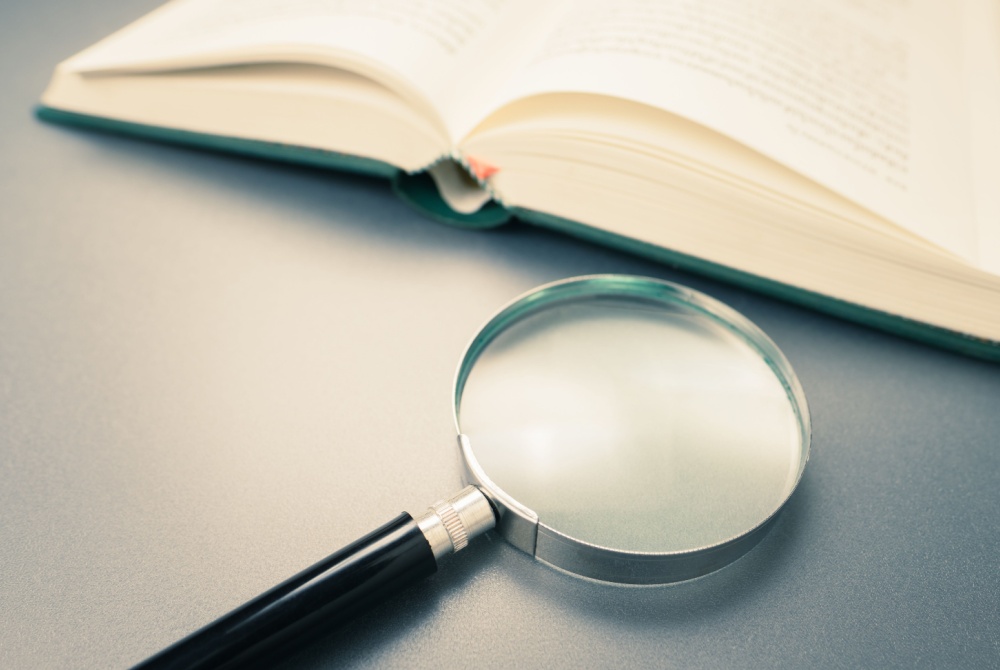 An open book on a table beside a magnifying glass
