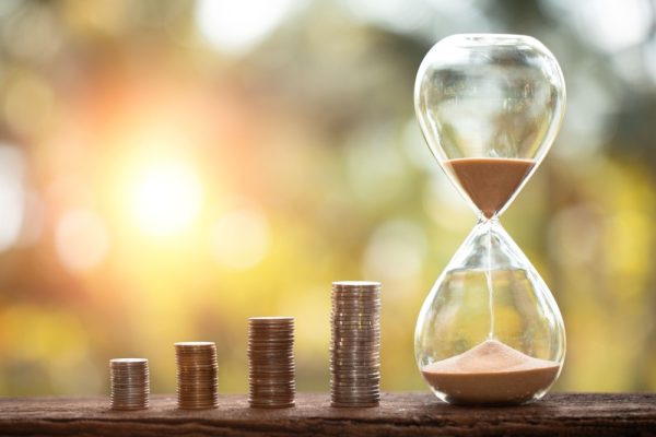 Piles of stacked coins next to an hourglass against a blurred sunset background.