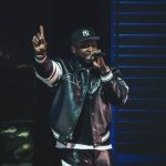 Rapper 50 Cent performs wearing a New York Yankees hat and leather jacket against a dark background