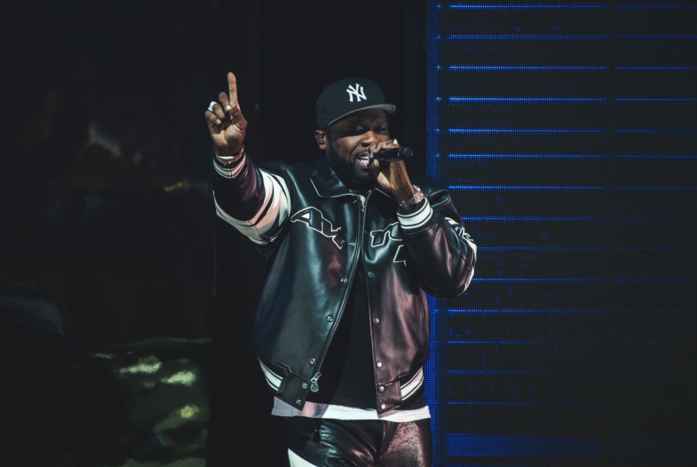 Rapper 50 Cent performs wearing a New York Yankees hat and leather jacket against a dark background