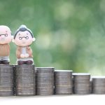 Senior couple and stack of coins on natural green background.