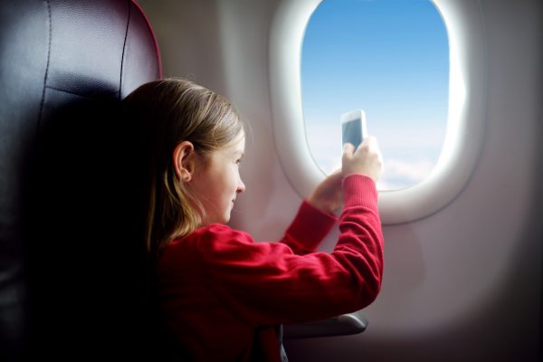 Girl in red shirt taking a phone picture while looking at the sky through an airplane window.