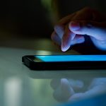 Article Banner - Man's hand hovering over smartphone lying on a table, against a dark background.