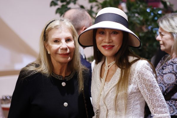 Yasmin Aga Khan, in black, stands to the left of Lucia Hwong Gordon, in white with a white hat.